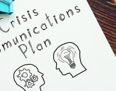 Piece of paper with "crisis communications plan" written on it and illustration of heads with gears and lightbulbs