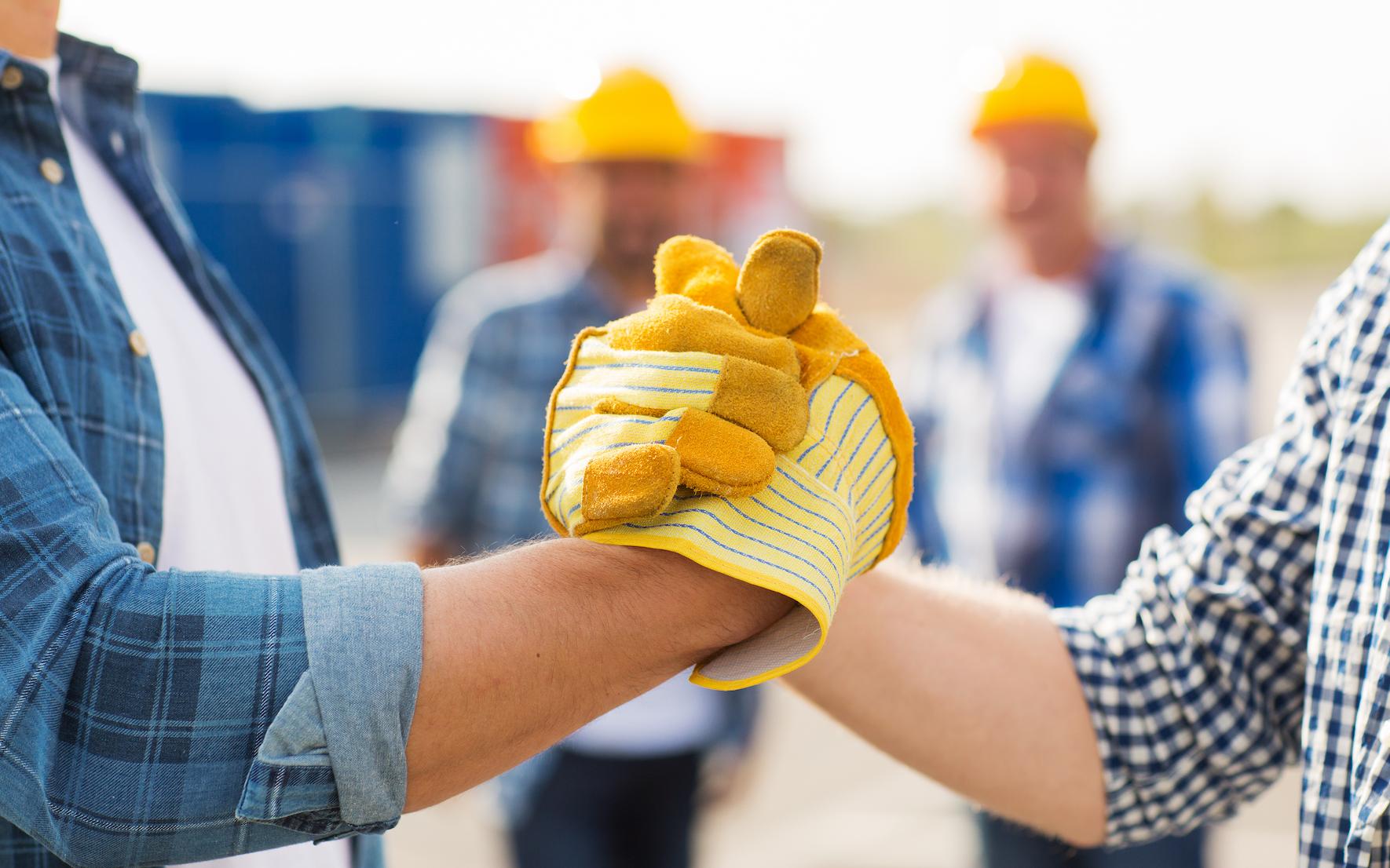 Two people wearing work gloves grip hands