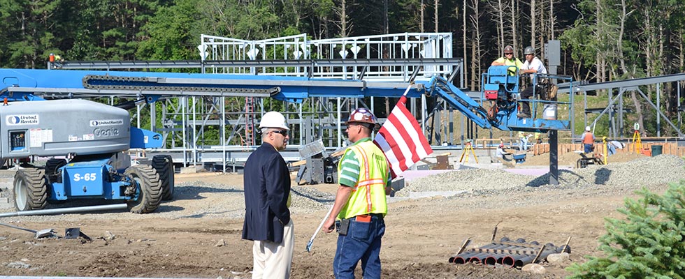 Two men are on a construction site, talking in front of a piece of machinery