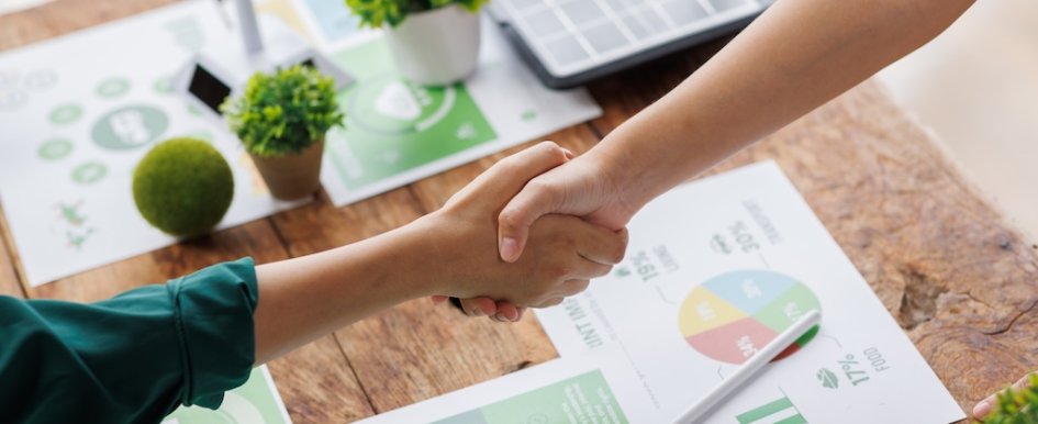 Handshake above eco-themed financial documents