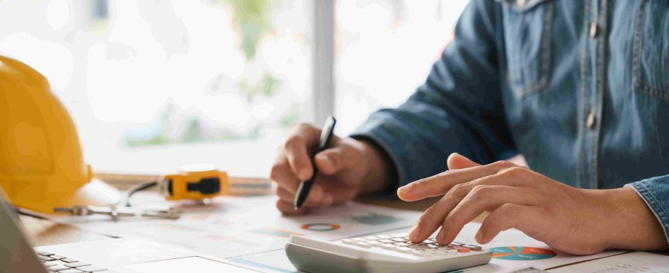 hands working with calculator and papers, hardhat in background