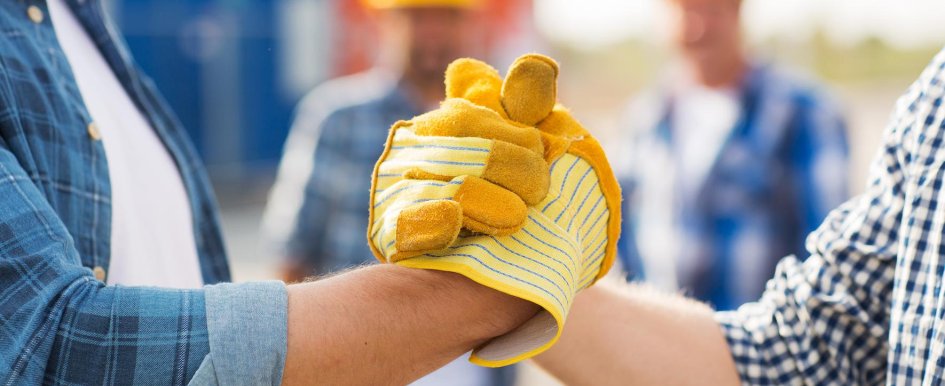 Two people wearing work gloves grip hands