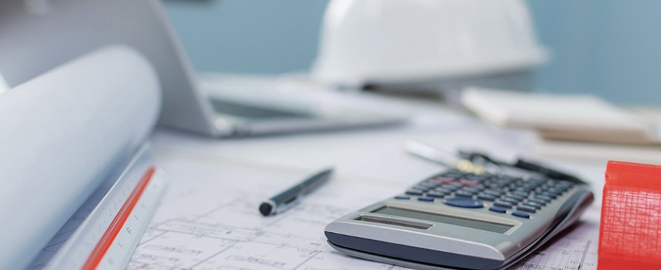 calculator on top of blueprints with hard hat in the background 