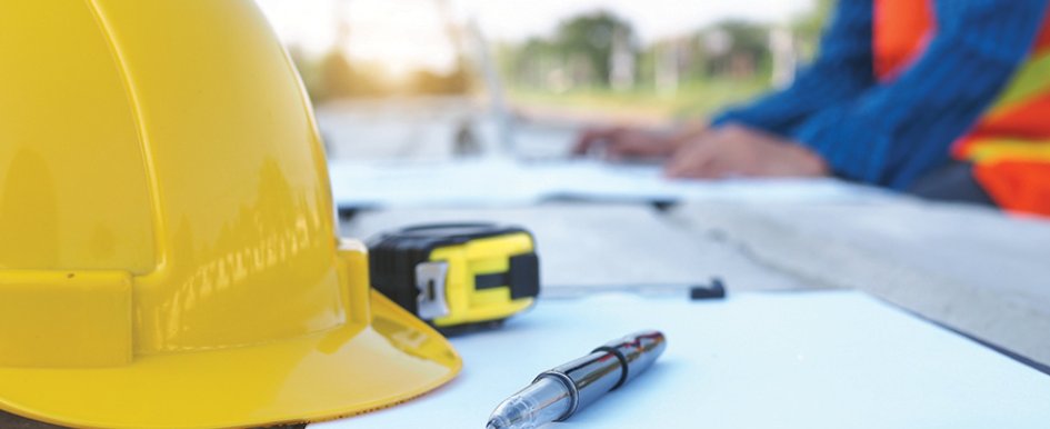 Hard hat and pen on a paper representing construction contracts / Adobe Stock