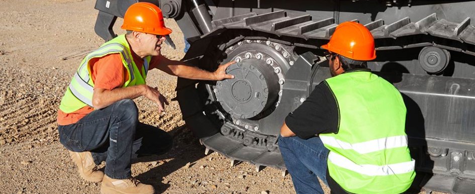 Two men in hard hats and vests inspecting dozer 