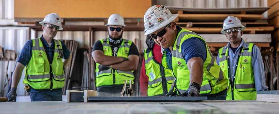 5 workers in green vests and white hard hats 