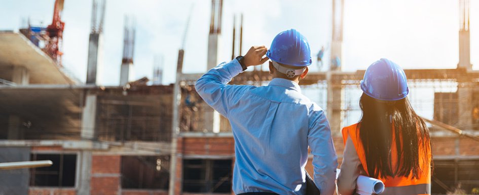 Two people in vests and hard hats looking at jobsite