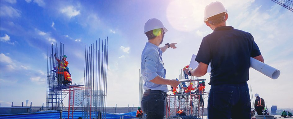 Two workers on jobsite; pointing to scaffolding with workers in the background