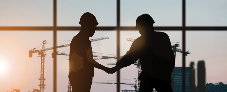Two workers in hard hats shaking hands/Adobe Stock