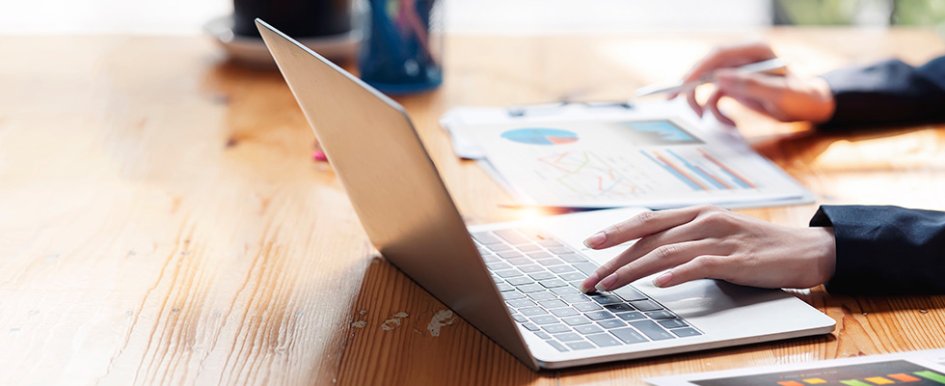 Person working on laptop while marking paper with graphs