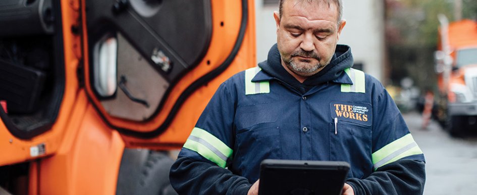 Man in work clothes standing in front of bright orange vehicle