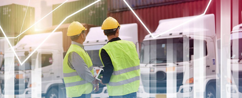 Two construction workers in hard hats and vests look at vehicle fleet / Adobe Stock