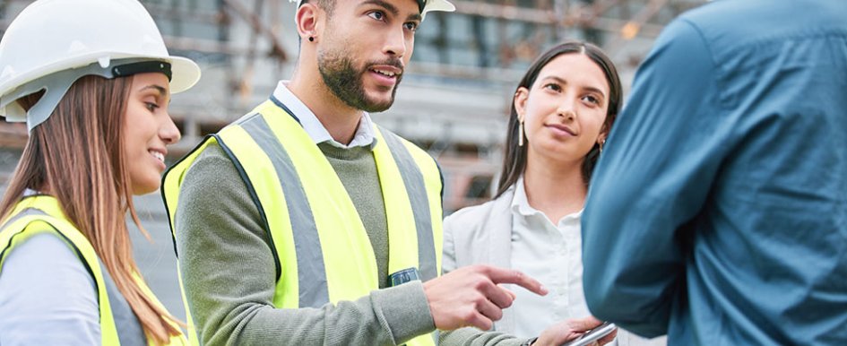 Workers in vests and hard hats gesturing toward phone and talking