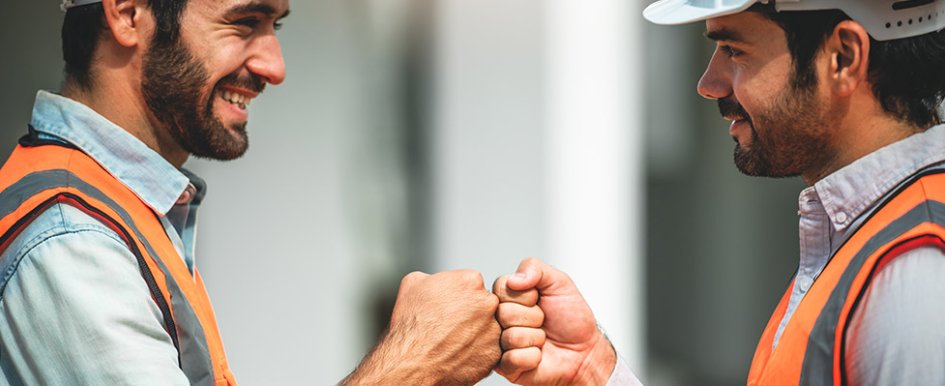 Two workers in vests and hard hats fist bumping