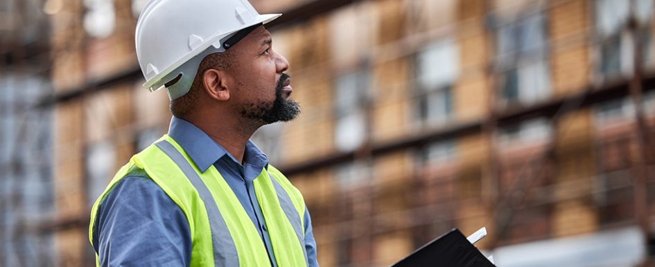 Worker in hardhat and green vest looking at building