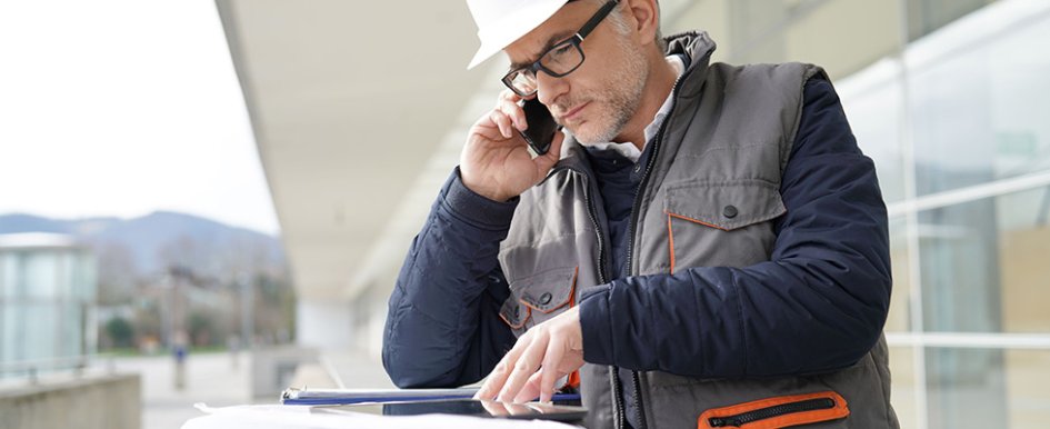 Man in hard hat on phone, looking at plans