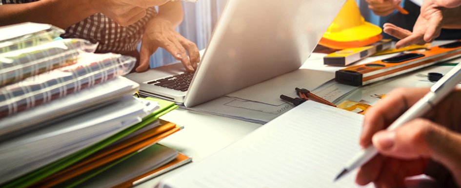 People working around desk with notebooks stacked beside laptop