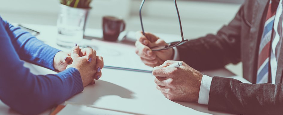 Two people sitting at desk in conversation 