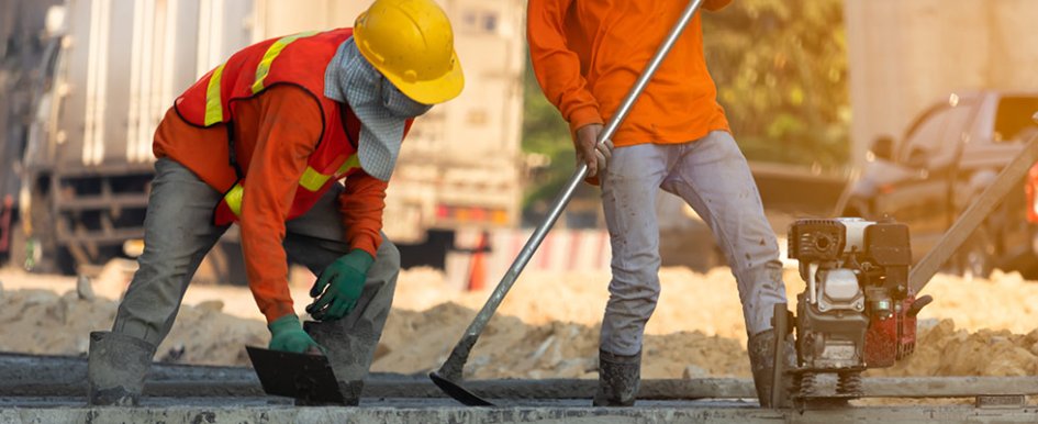 Two workers in orange construction vests and hard hats working on concrete