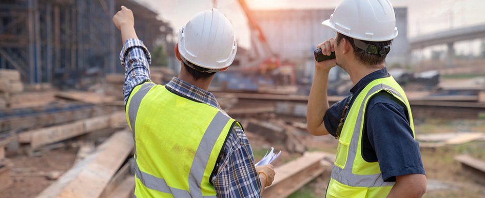 Two construction workers on a jobsite, one pointing forward