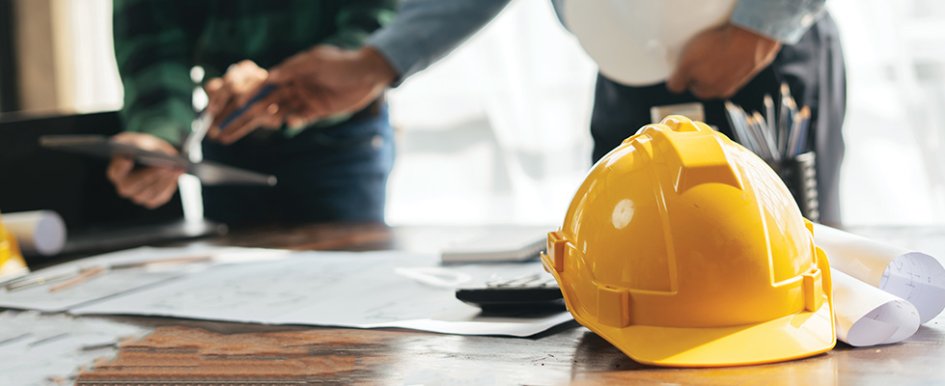 hard hat and papers on a desk to represent job costing/Adobe Stock