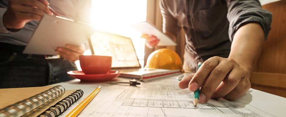 Hands of two workers at desk with hard hat in background