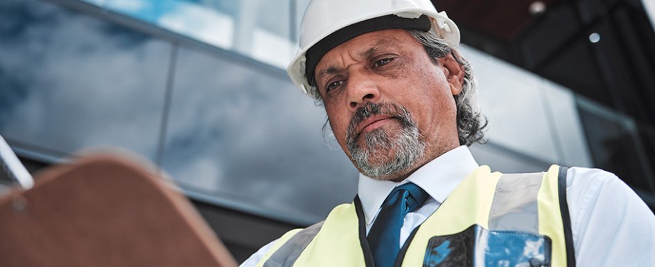 Man in hard hat and vest looking at clipboard