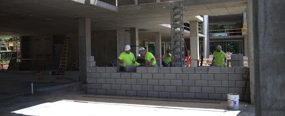 Workers in green shirts and hard hats working on wall