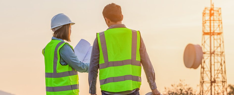 Man and woman in construction vests and hardhat looking at papers on jobsite