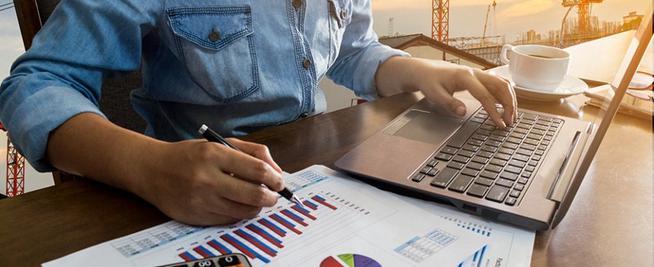 Person seated at desk, using a laptop and looking at charts