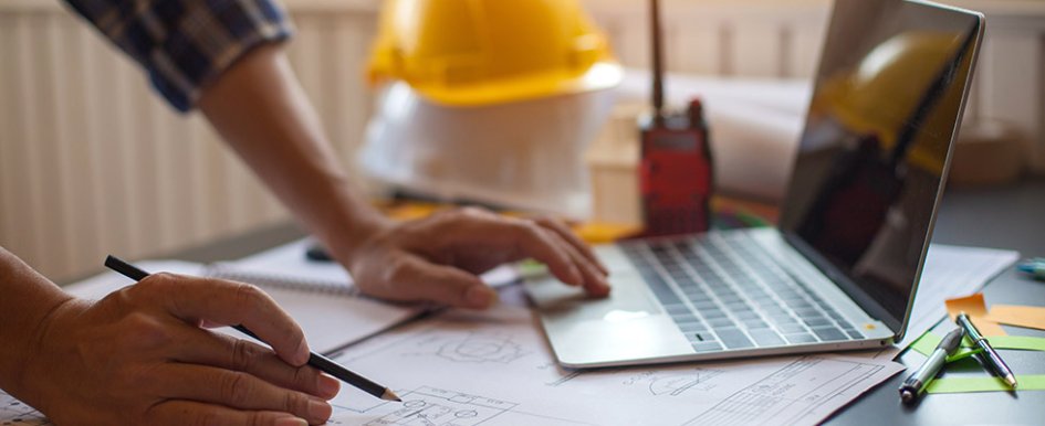 Hands in front of laptop with hard hat in background