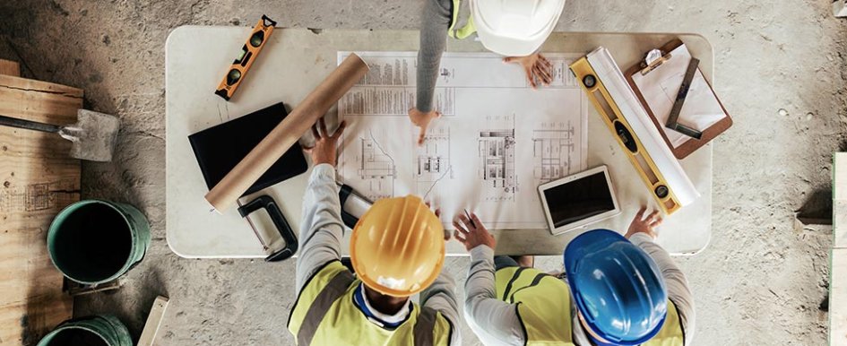 Three people in hard hats looking at plans