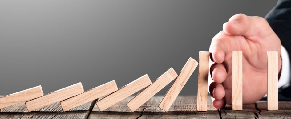 risk mitigation as demonstrated by a hand stopping falling dominoes