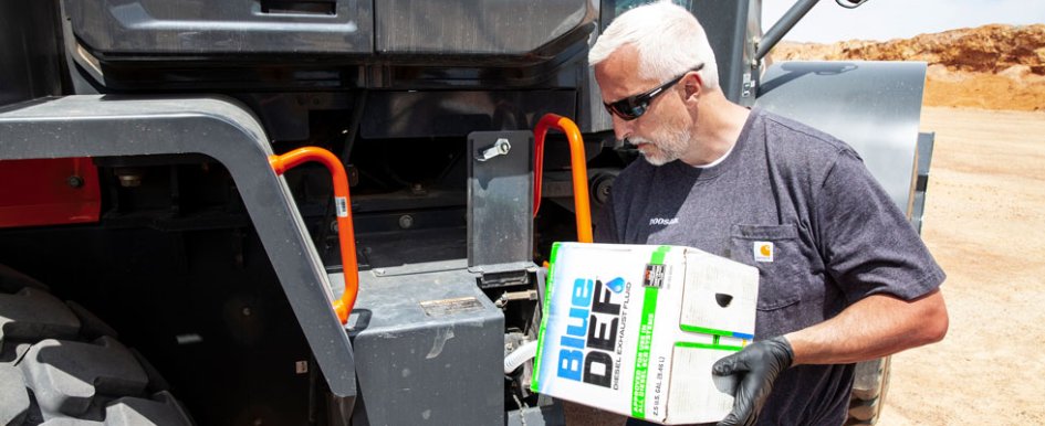 Man pours diesel exhaust fluid into a large piece of equipment