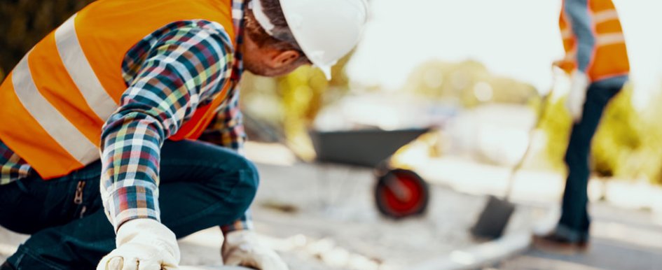 A person in a hard hat and bright orange safety vest looks at a road construction site