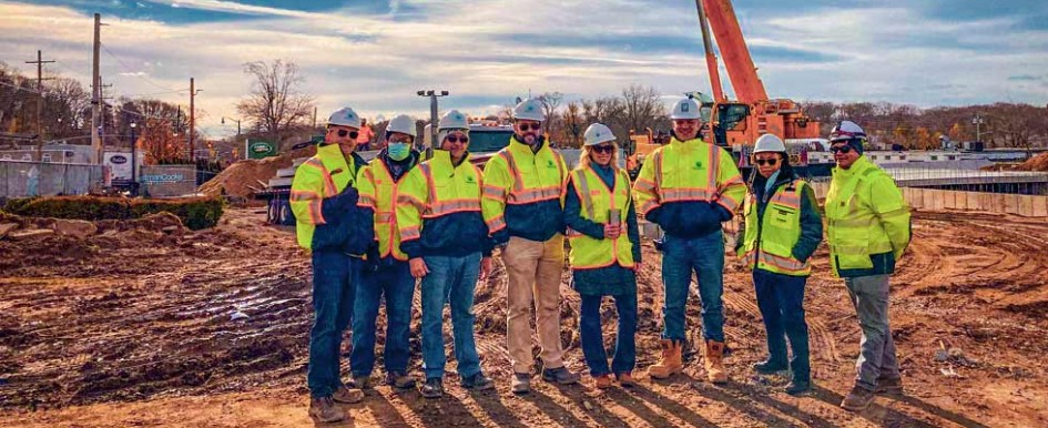 Eight people in bright safety jackets stand on a construction site