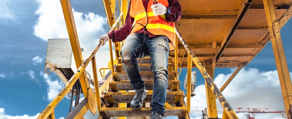 A person wearing jeans and a bright safety vest descends metal stairs holding the railing with one hand