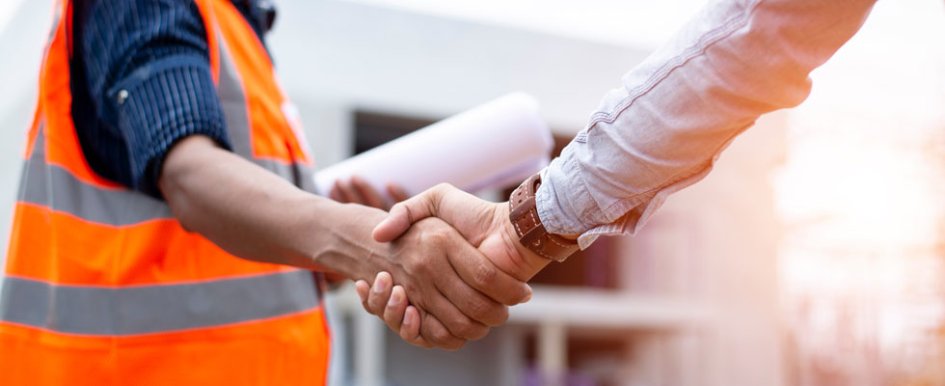 A person in a bright safety vest, holding paper in one hand, shakes hands with someone in a long sleeve shirt.