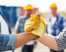 Two people wearing work gloves grip hands