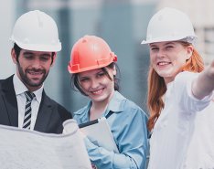 Three construction workers in hard hats smiling and looking at blueprints