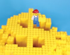 Lego blocks in the shape of a dollar bill with a Lego construction worker on top / Adobe Stock 