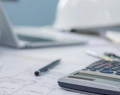 calculator on top of blueprints with hard hat in the background 