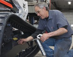 Man checking Bobcat machine's tracks/Bobcat