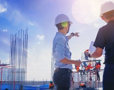 Two workers on jobsite; pointing to scaffolding with workers in the background