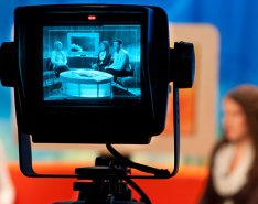 A camera display shows a group of three people on a TV talk show