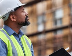 Worker in hardhat and green vest looking at building
