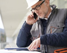 Man in hard hat on phone, looking at plans