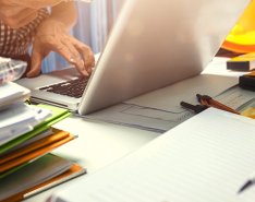 People working around desk with notebooks stacked beside laptop