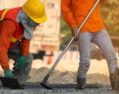 Two workers in orange construction vests and hard hats working on concrete