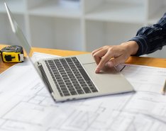 Hands using laptop on desk with hard hat, tablet, measuring tape and tools